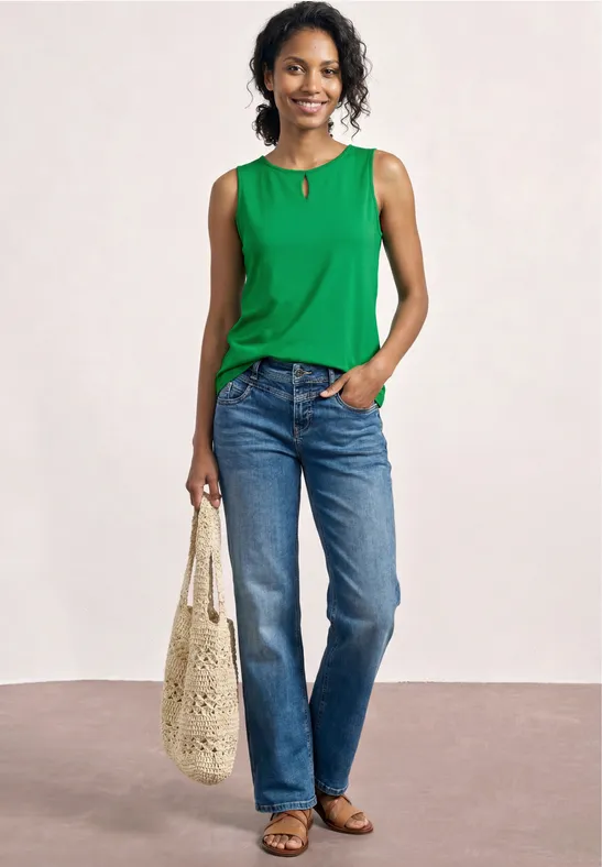 Vrouw in groen mouwloos topje, blauwe jeans, sandalen en beige nettas.
