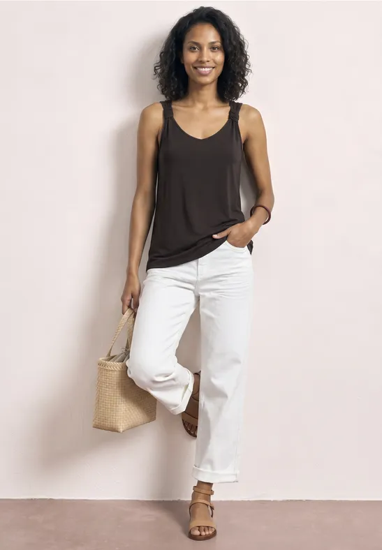 Frau in schwarzem Top und weißen Jeans, mit Strohtasche.