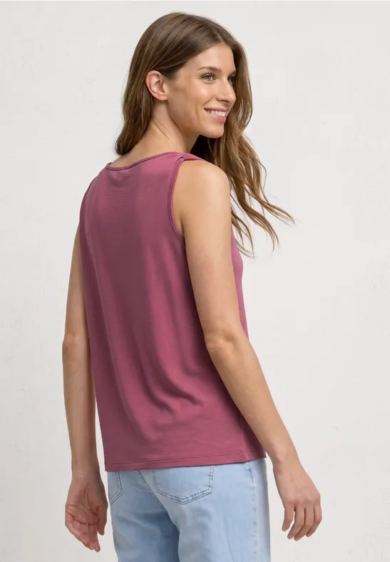 Vrouw van achteren in een mouwloos bordeaux topje en lichtblauwe jeans, losse pasvorm en los haar.