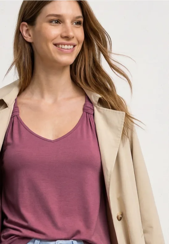 Vrouw in een roos mouwloos topje en een lichtbeige jas.