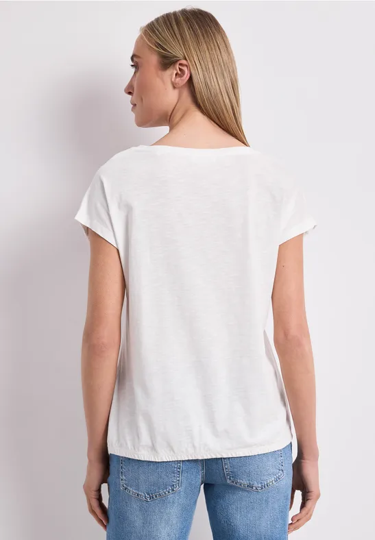 Frau von hinten in weißem T-Shirt und blauen Jeans vor hellem Hintergrund.