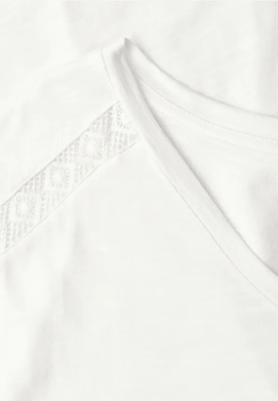 Nahaufnahme eines weißen T-Shirts mit Spitzenbesatz an der Schulter und Rundhalsausschnitt.