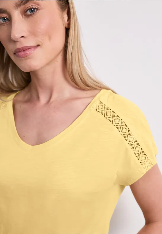 Frau in gelbem Shirt mit kurzen Ärmeln und Spitzenbesatz auf der Schulter.