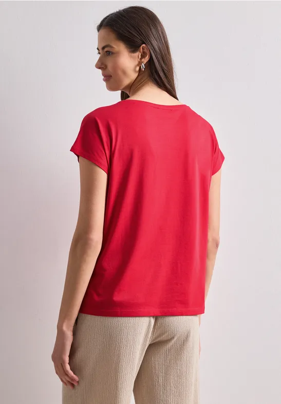 Vrouw van achteren met een eenvoudige rode T-shirt en beige broek voor een neutrale achtergrond.