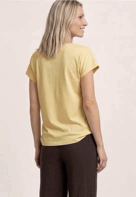 Achteraanzicht van een blonde vrouw in geel T-shirt en bruine broek voor lichte achtergrond.
