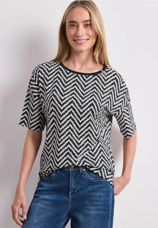Frau in schwarz-weißem Zickzack-Shirt und blauen Jeans, eine Hand in der Tasche