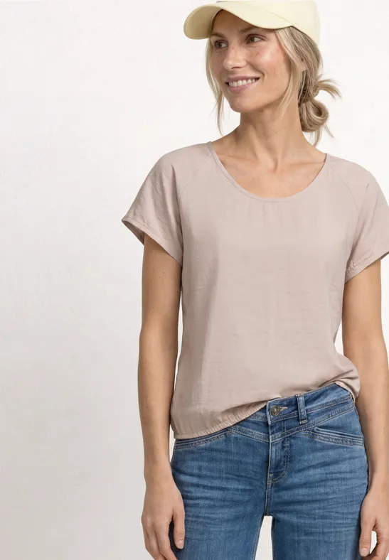 Jeune femme portant un t-shirt beige et un jean bleu sur fond neutre.