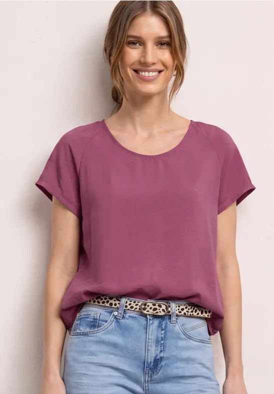 Vrouw in paarse top met korte mouwen, spijkerbroek en luipaardriem.