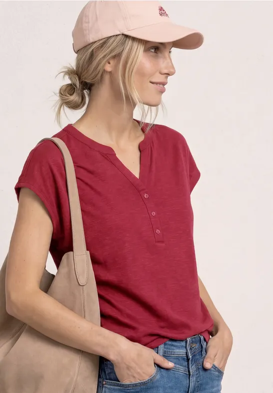 Vrouw met rood kort shirt, roze pet en beige schoudertas voor een lichte achtergrond.