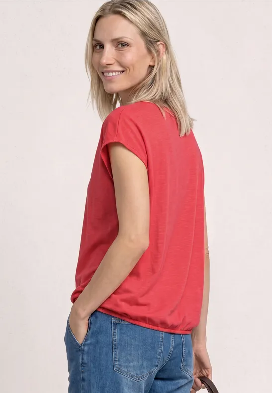Seitliche Ansicht einer Person in rotem T-Shirt und Jeans, Hand in der Tasche