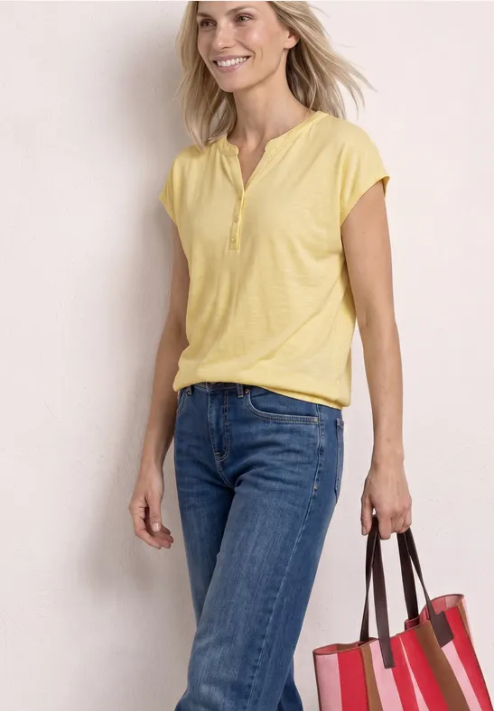 Eine Frau in gelbem Oberteil und Jeans trägt eine große rote Tasche.