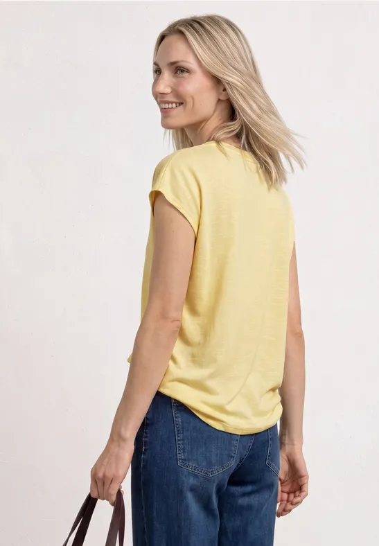 Eine Frau von hinten in gelbem T-Shirt und blauen Jeans, die eine Handtasche hält.