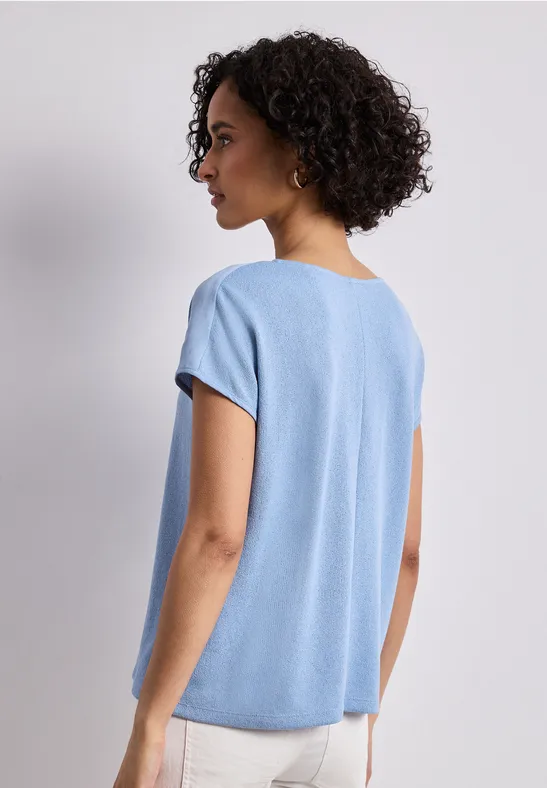 Vrouw van achteren in loszittend lichtblauw T-shirt, kort gekruld haar