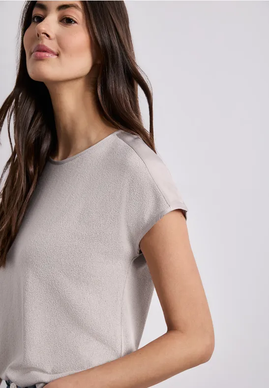 Frau im cremefarbenen, locker sitzenden T-Shirt mit kurzen Ärmeln vor neutralem Hintergrund.