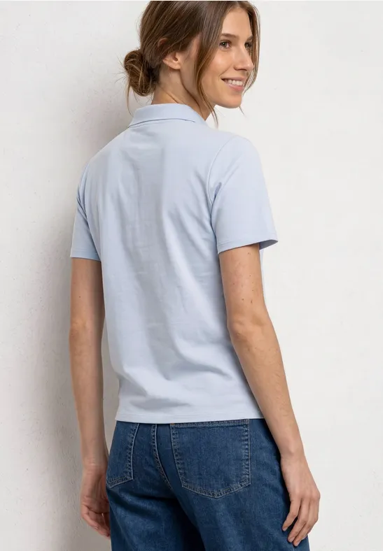 Vrouw van achteren in lichtblauw poloshirt en spijkerbroek met knot.