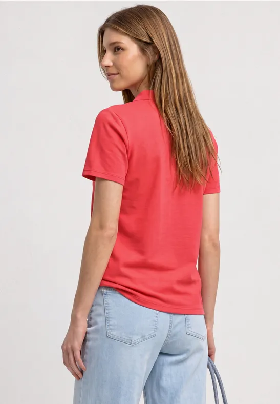 Frau von hinten in rotem T-Shirt und hellblauen Jeans, trägt Handtasche.