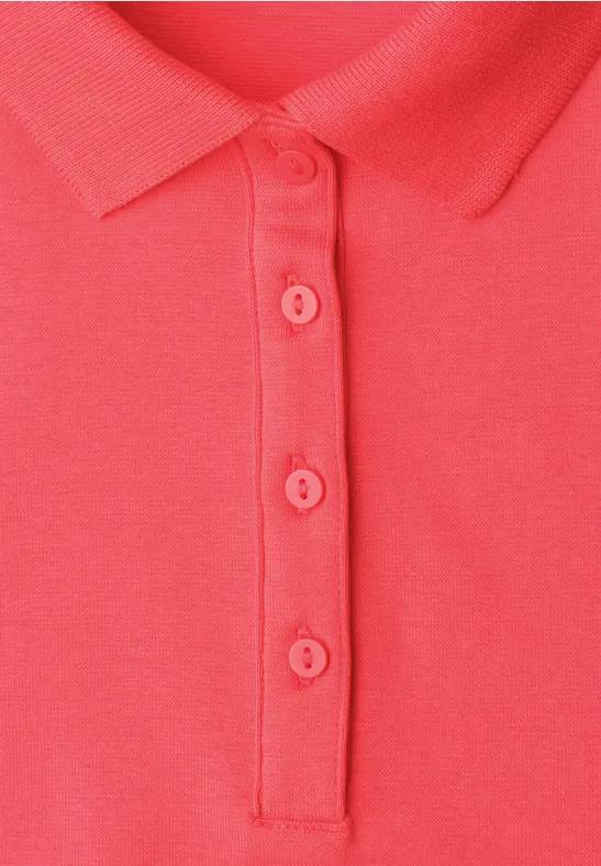 Nahaufnahme eines korallroten Poloshirts mit Kragen und vier Knöpfen.