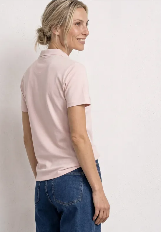 Vrouw van achteren in een roze T-shirt en blauwe jeans tegen een effen lichte achtergrond.