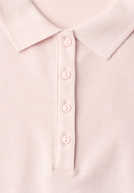 Close-up van een pastelroze poloshirt met kraag en vier knopen.