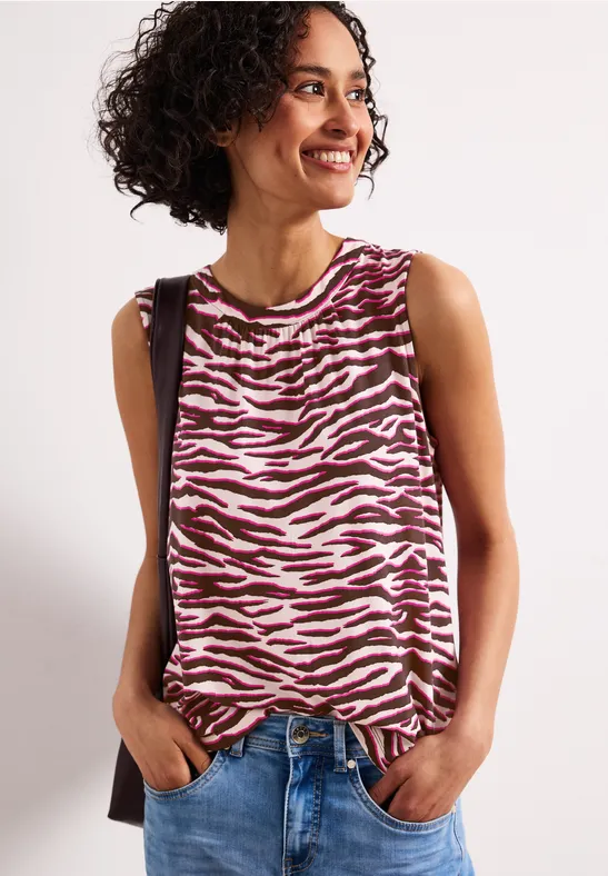 Vrouw met roze-wit zebramotief tanktop, jeans, schoudertas, handen in de zakken.