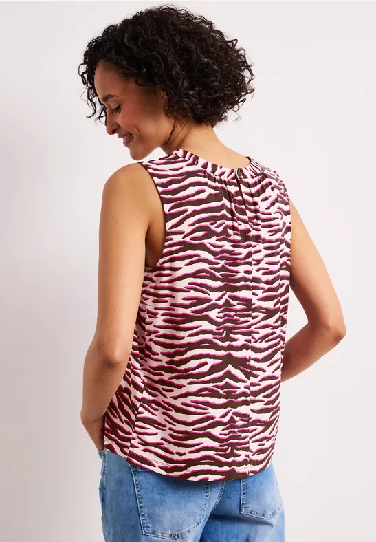 Persoon rugzijde in een mouwloos roze-wit zebraprint top en blauwe spijkerbroek.