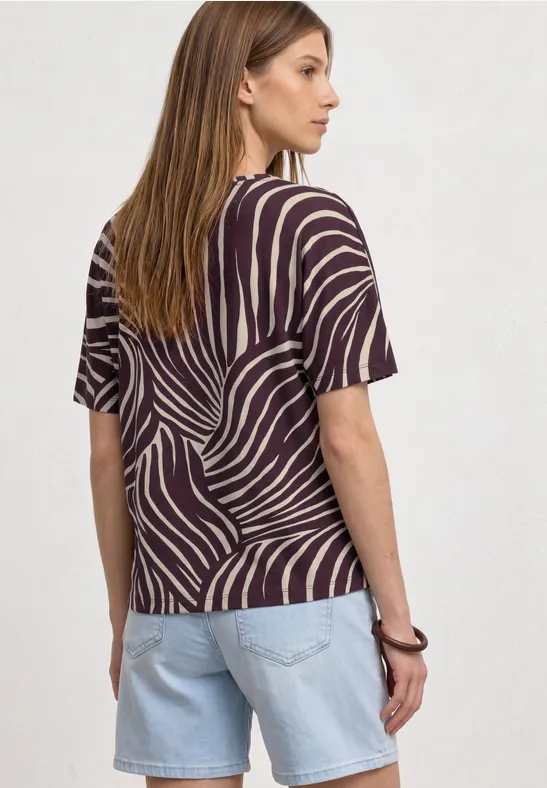 Eine Frau von hinten mit gestreiftem Zebra-Muster-Shirt und hellen Jeans-Shorts, braune glatte Haare.