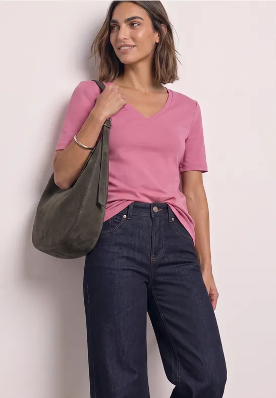 Frau trägt rosa T-Shirt, dunkelblaue Jeans und hält eine olivgrüne Tasche.