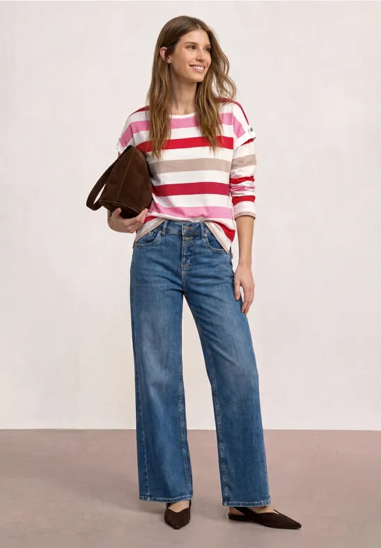 Vrouw in roze-wit gestreepte trui, wijde jeans, zwarte pumps en bruine schoudertas.