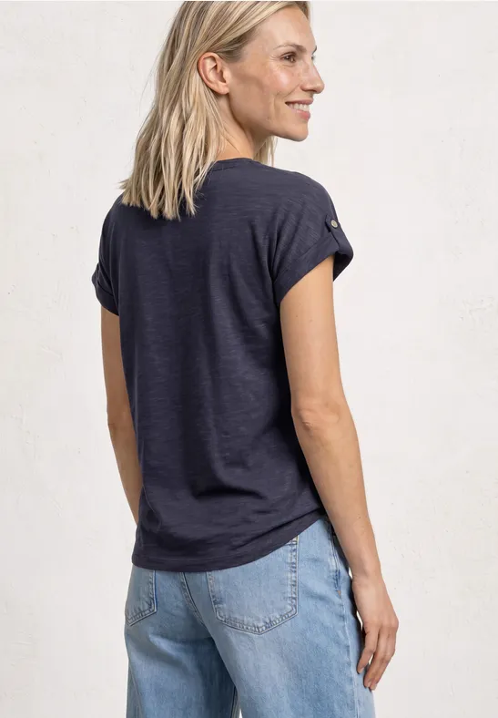 Een vrouw van achteren in een donkerblauw T-shirt en lichte jeans, voor een lichte achtergrond.