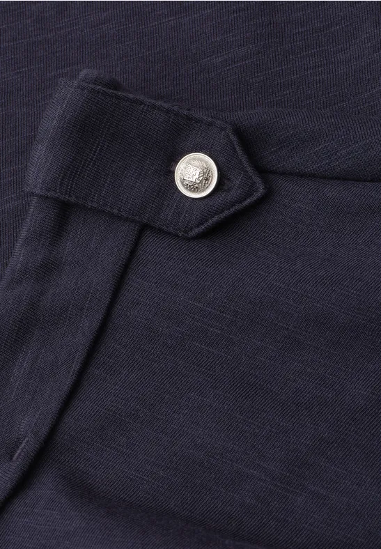 Detail van een donkerblauwe stoffen broek met een zilverkleurige drukknop op de klep