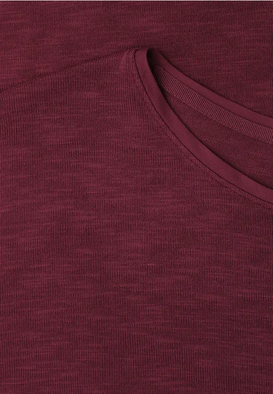 Close-up van een donkerrood T-shirt met ronde hals en subtiel gemêleerde stof.