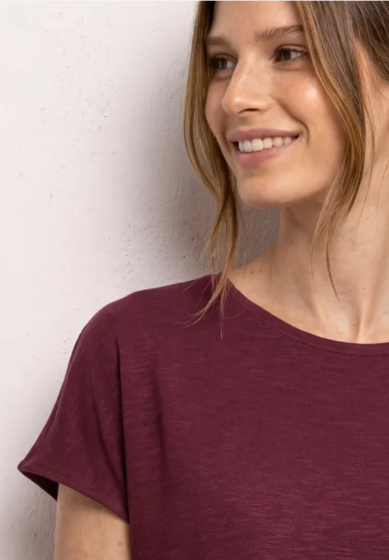 Vrouw in bordeaux T-shirt met gouden ringoorbel, gezicht vervaagd