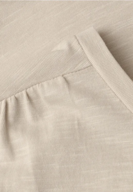 Close-up van een beige stof met een ingestikte zak en zichtbare naden.