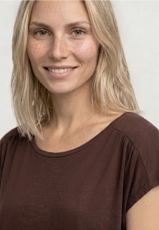 Blondynka w brązowej koszulce na jasnym tle.