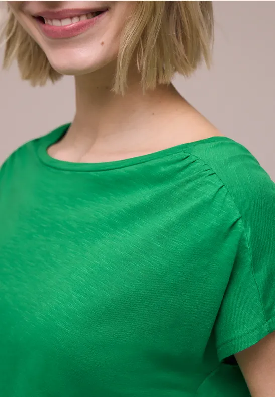 Nauw portret van vrouw in groen shirt met een subtiele glimlach.