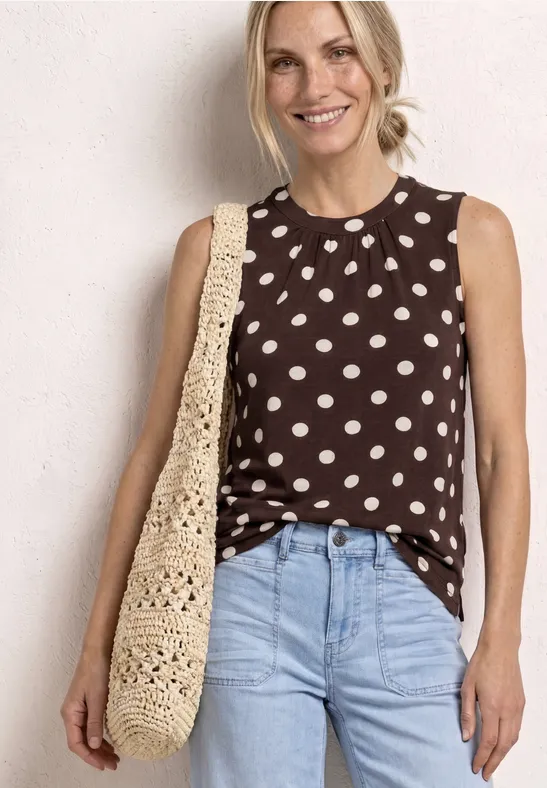 Frau in braunem, ärmellosem Polka-Dot-Top, hellblauer Jeans und gehäkelter Schultertasche