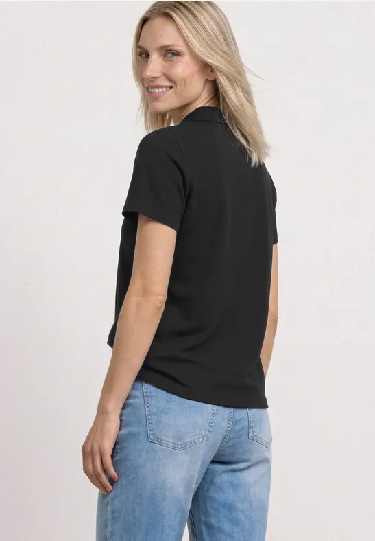 Een vrouw in zijaanzicht draagt een zwart t-shirt en blauwe spijkerbroek voor een witte achtergrond.