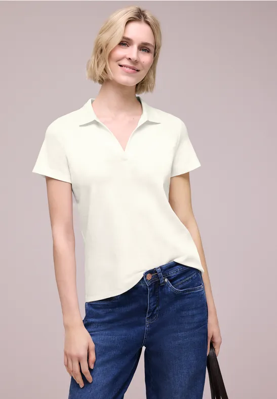 Vrouw in een wit poloshirt en blauwe jeans met een zwarte tas in de hand.