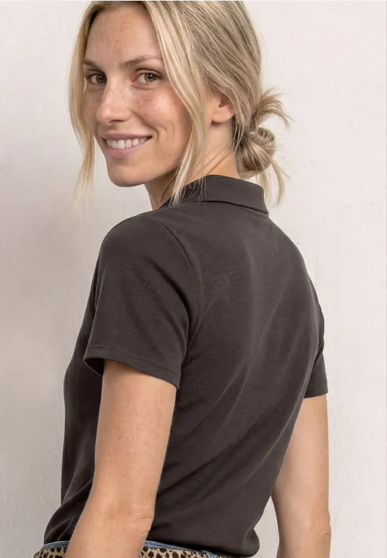 Vrouw in zwart T-shirt met korte mouwen, blond haar in knot, kijkend over haar schouder.