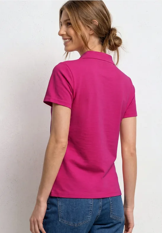 Vrouw van achteren in een felroze poloshirt en blauwe spijkerbroek, haar in een losse knot.