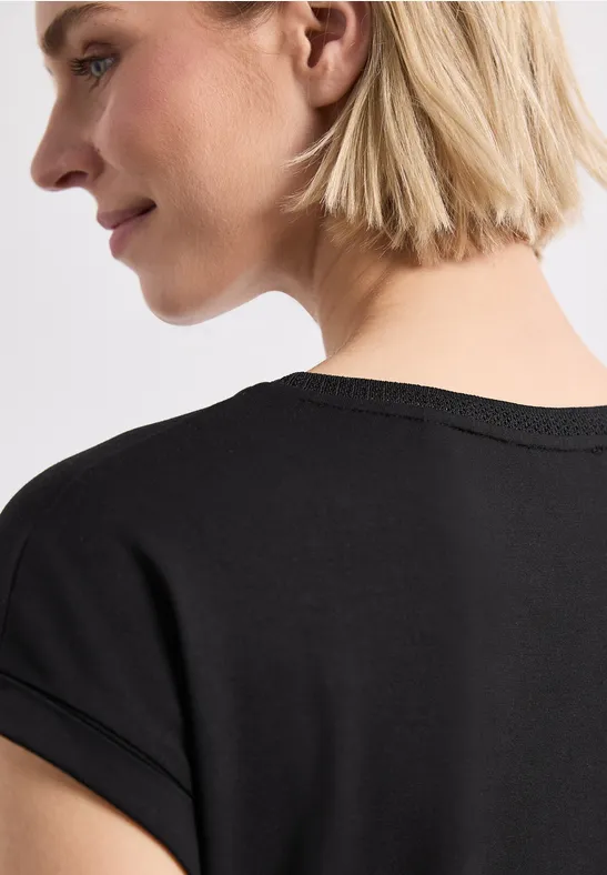 Rückansicht einer Person mit kurzem, blondem Haar, die ein schwarzes T-Shirt trägt.