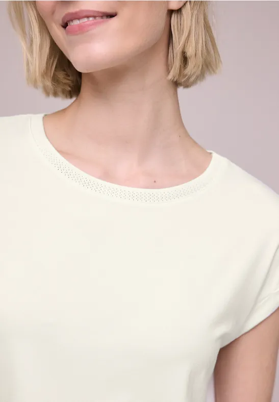 Ausschnitt einer lächelnden Frau in hellem T-Shirt, nur Oberkörper zu sehen.