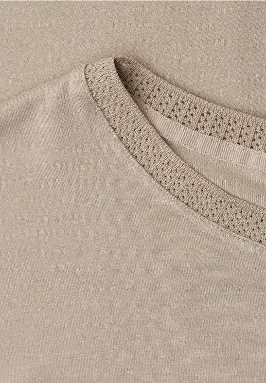 Nahaufnahme eines cremefarbenen T-Shirts mit zartem Häkel-Spitzenbesatz am Kragen.