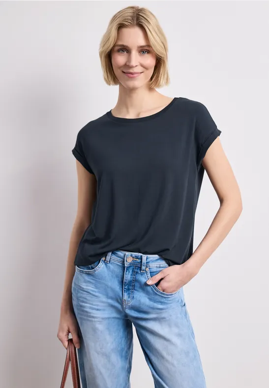 Vrouw in donkerblauw T-shirt en lichte spijkerbroek, met een handtas.