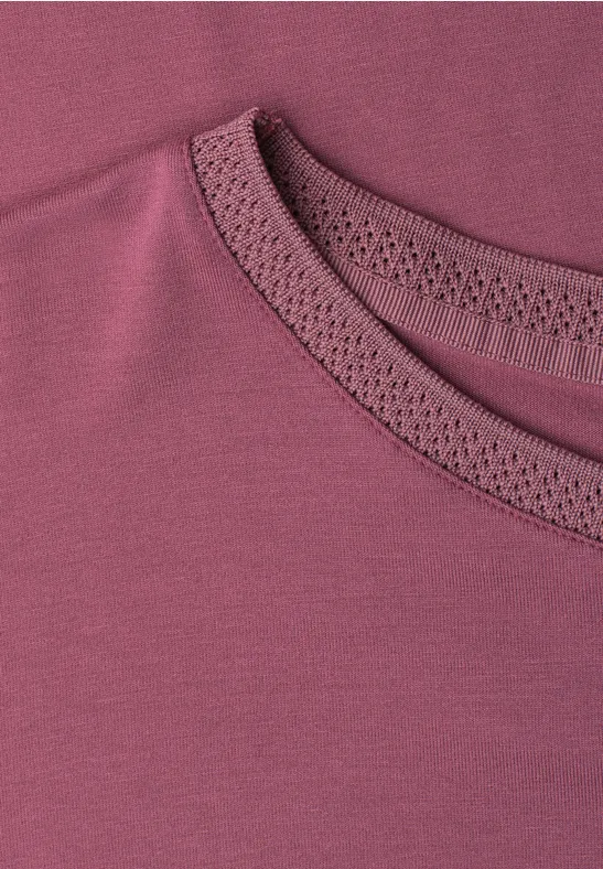 Nahaufnahme eines weinroten Shirts mit zierlicher Lochspitze am Rundhalsausschnitt.