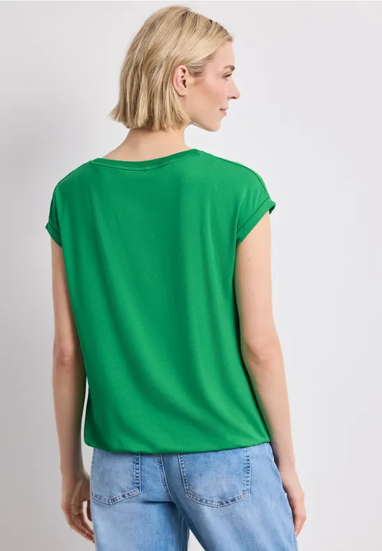 Frau mit kurzärmligem grünen Oberteil und Jeans, Rückenansicht.