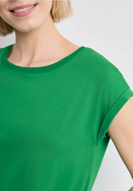 Teil eines lächelnden blonden Models in grünem T-Shirt vor hellgrauem Hintergrund.