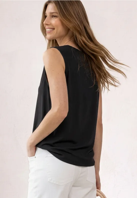 Vrouw van achter gezien met een zwart mouwloos shirt en witte jeans.