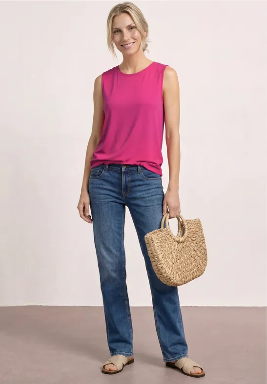 Frau in pinkem Top, blauen Jeans, trägt gewebte Basttasche.