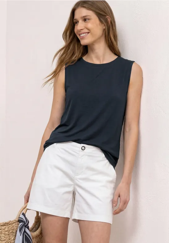Vrouw in mouwloos donkerblauw topje en witte short, met een strooien tas.